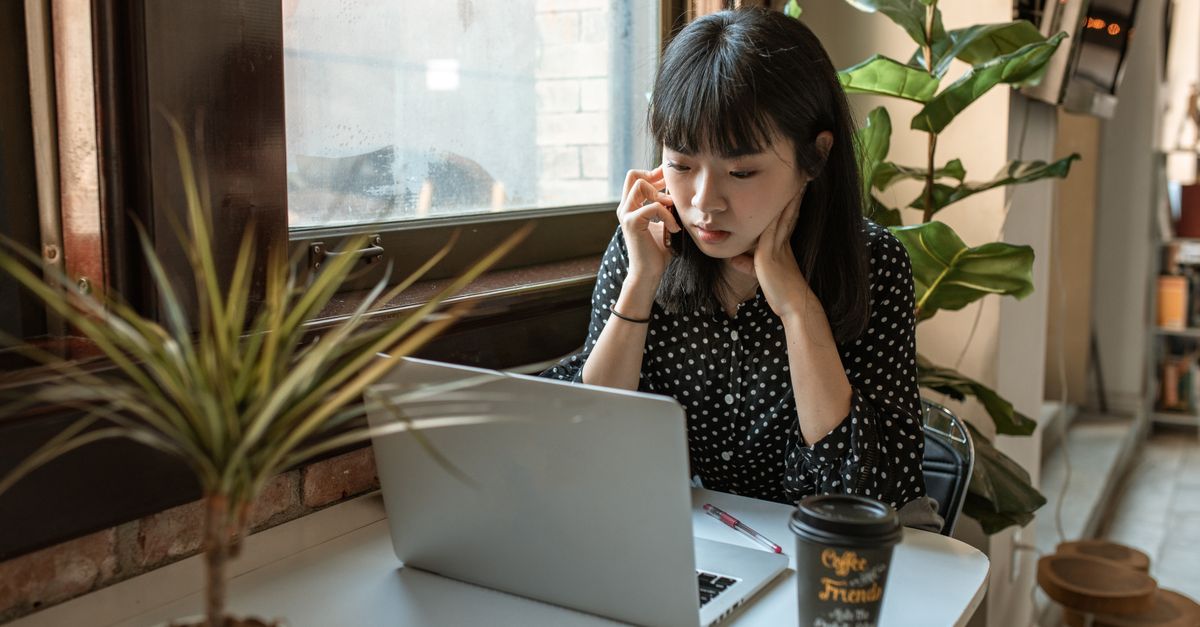 ノートパソコンを見ながら電話でサポートに問い合わせている女性